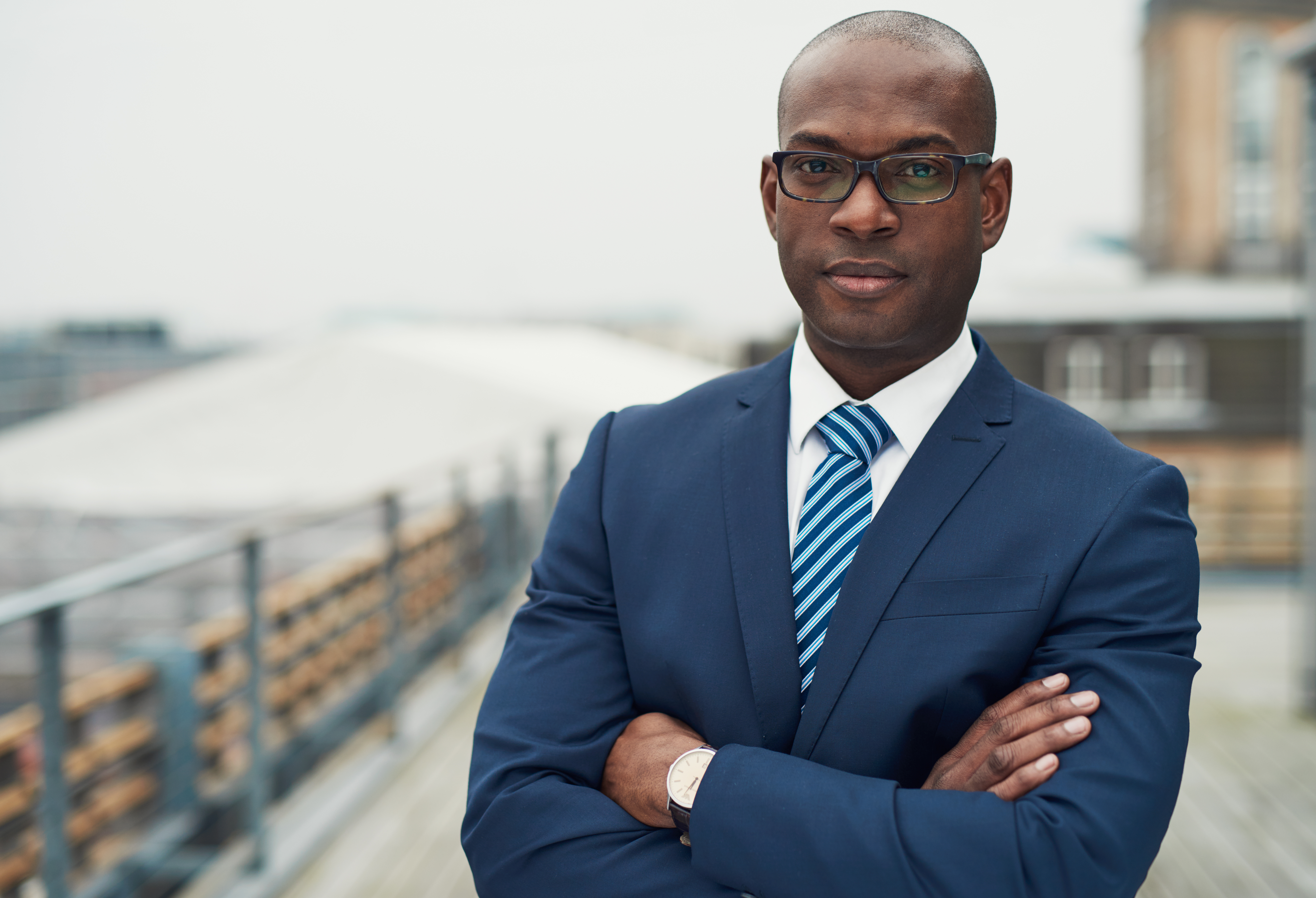 Picture of a mail black company director wearing a blue suit, white shirt, light tie and glasses.