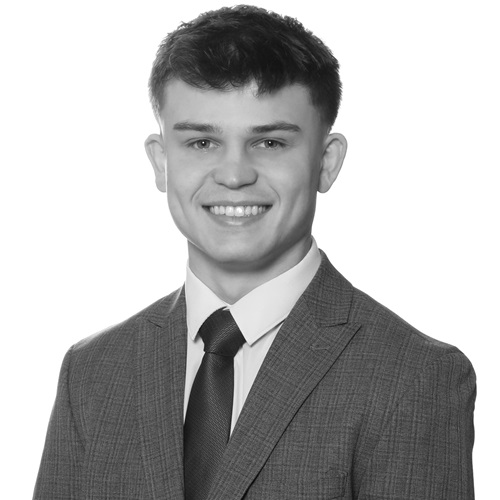 Finn Skinner. A Young man in a grey suit, dark tie and white shirt.